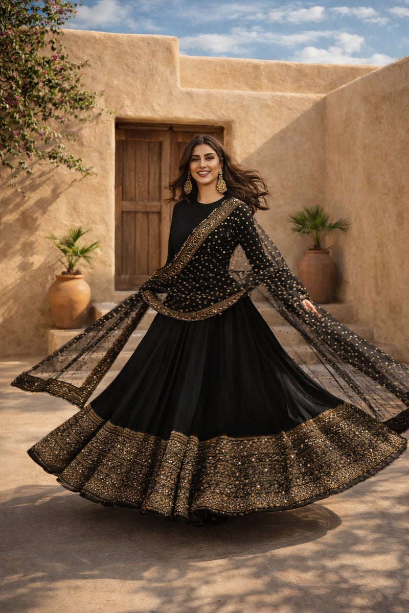 Woman in a black and gold traditional outfit standing in front of a beige building with plants.